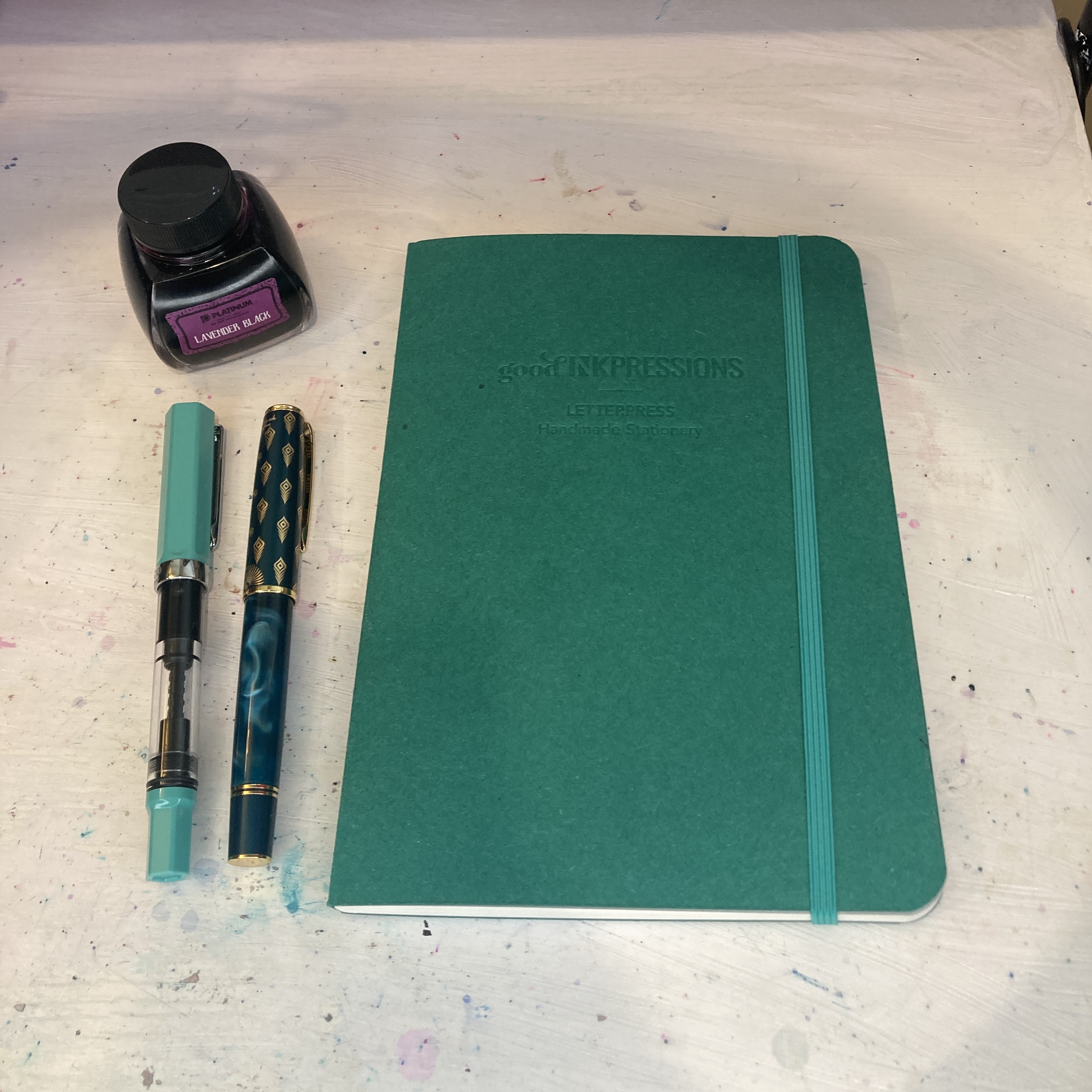 A bottle of ink, two fountain pens, and a teal-green A5 journal