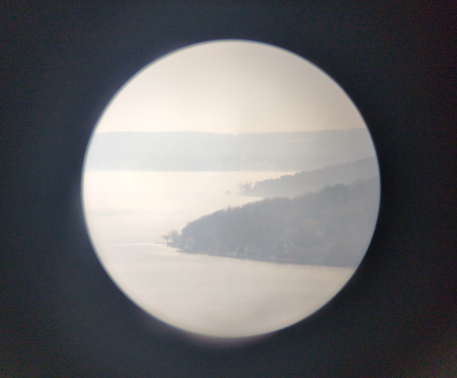 A misty lakeshore taken through a pair of binoculars. The image is inset as a small circle in the middle of a black background