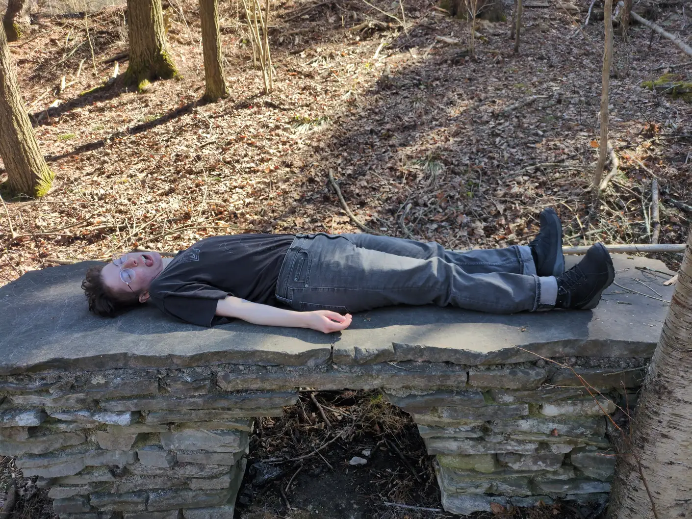 My partner lying down on a stone bench with their eyes shut and their tongue hanging out