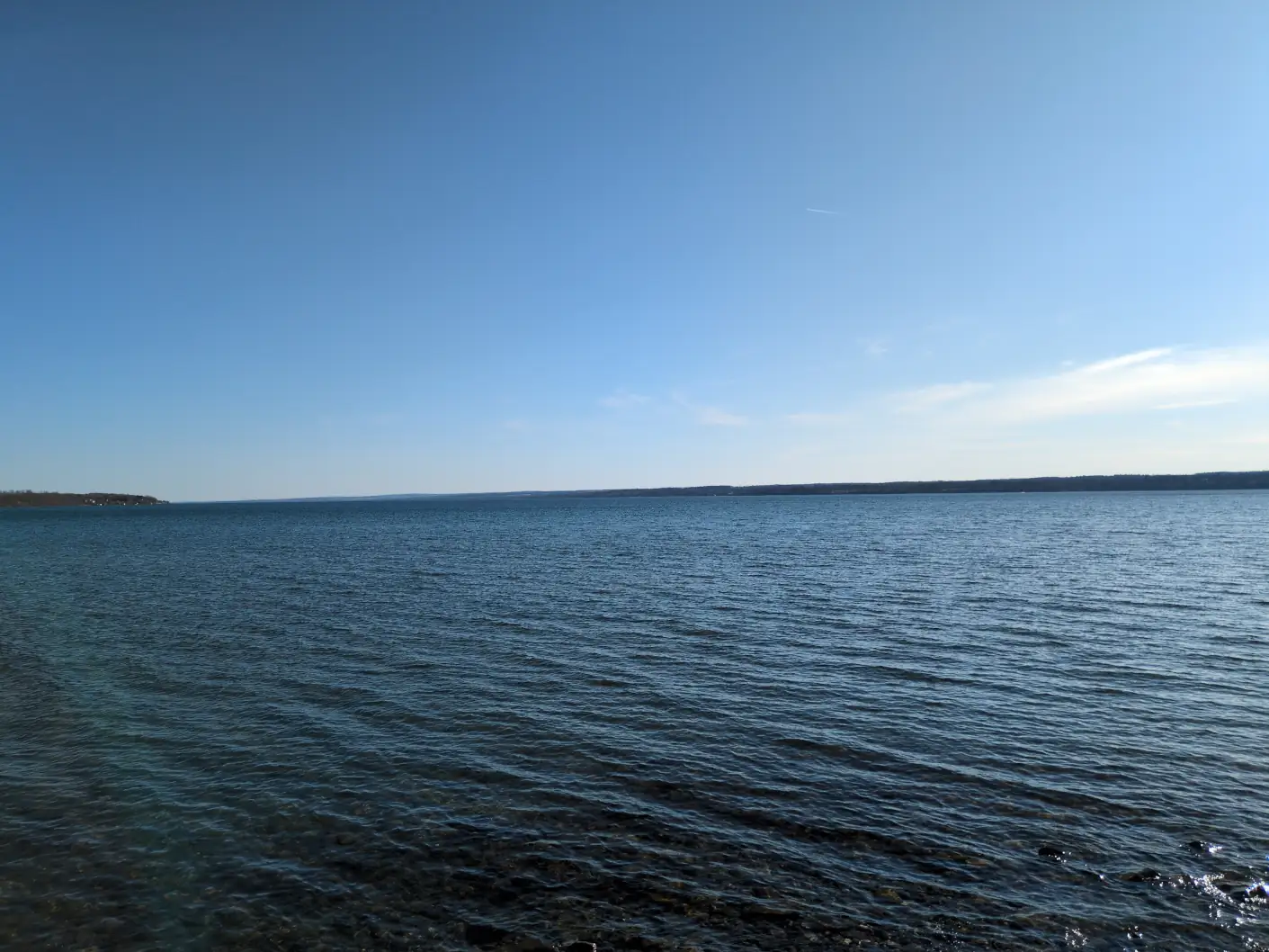 A clear blue lake in the late afternoon, with stones visible near the shore.