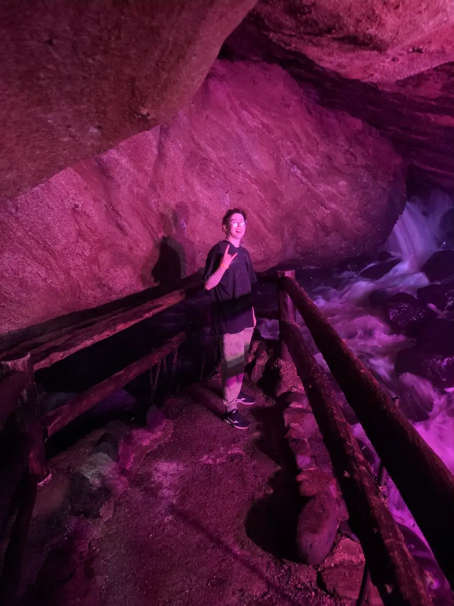 A person in a black T-shirt, sweats, and glasses (my partner) making a “rock-n-roll” hand gesture and sticking out their tongue